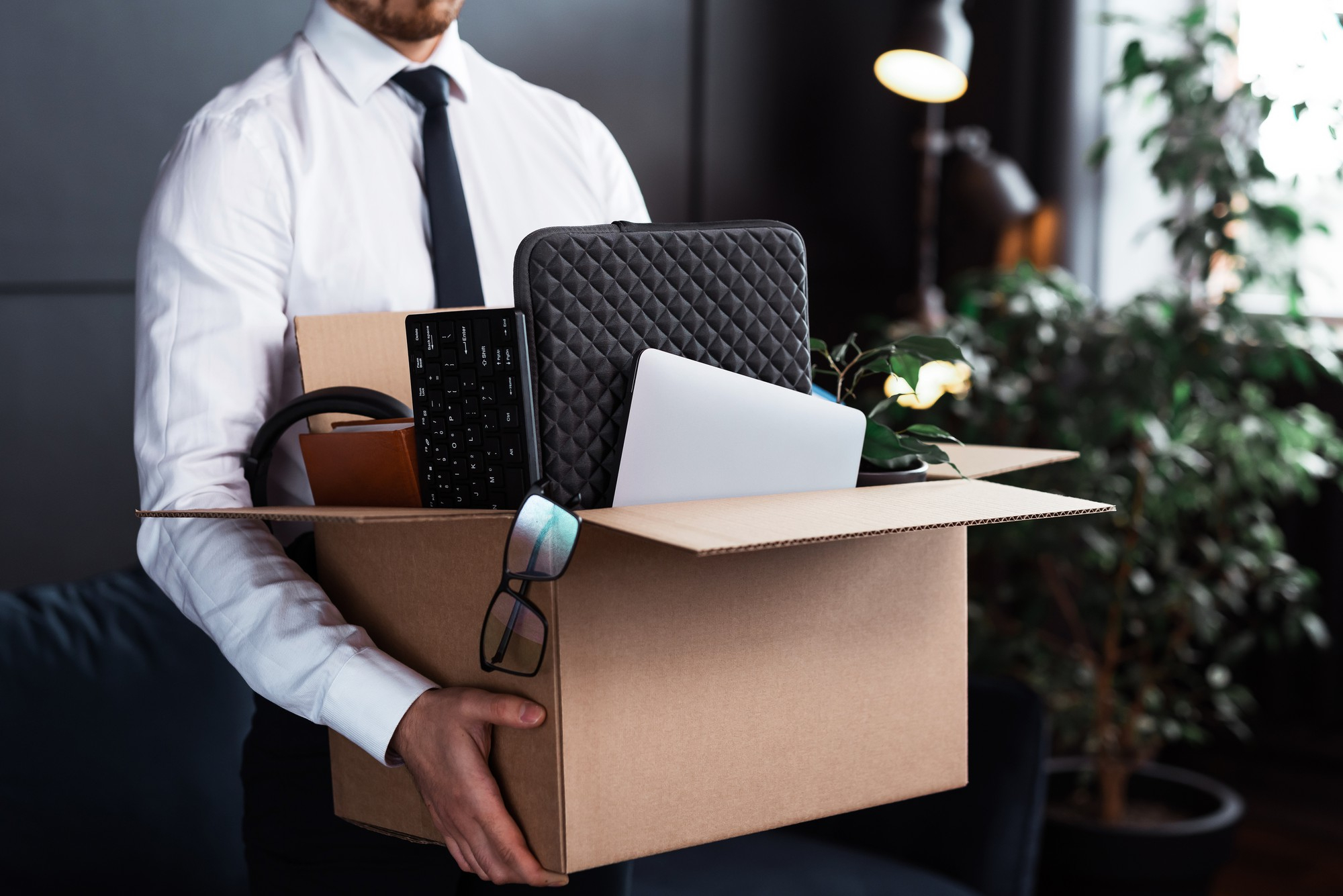 Young man walking out of office with box after layoff